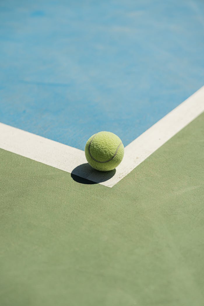 Close-up of a tennis ball positioned on the corner of a vibrant outdoor court.