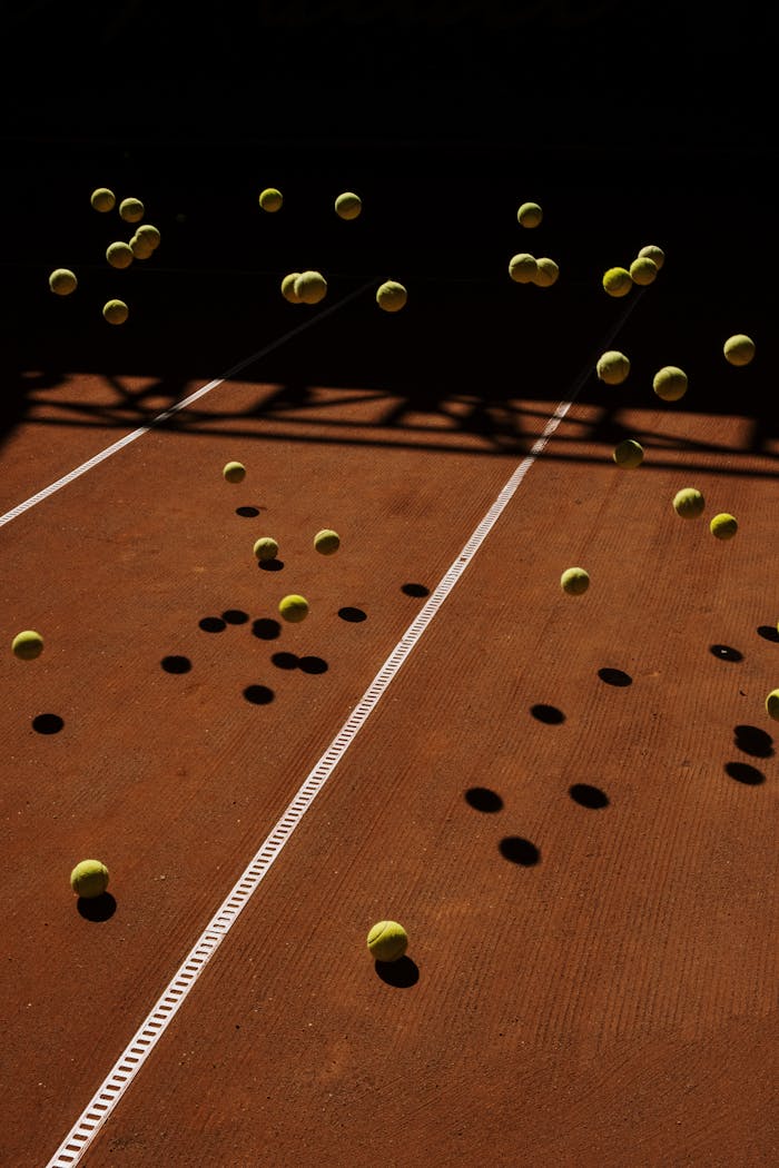 services-01 Tennis balls in mid-air on a clay court create a dynamic motion effect with dramatic shadows.